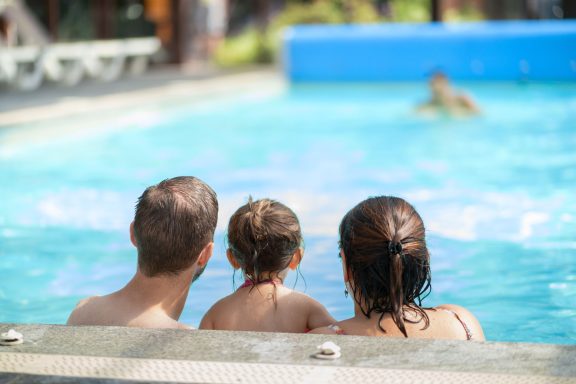 Trois personnes assises au bord d'une piscine, regardant quelqu'un nager.