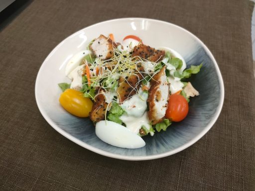 Salade avec poulet grillé, tomates cerises, légumes variés et sauce blanche.