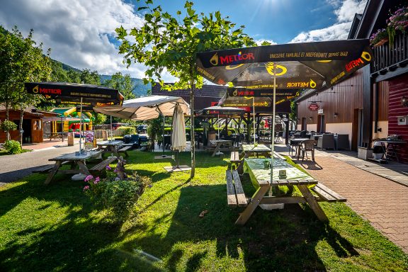 Terrasse du restaurant avec tables, chaises, et verdure environnante sous un ciel ensoleillé.