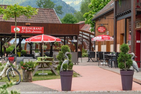 Terrasse de café avec parasols rouges et sculptures de hérons en pot.