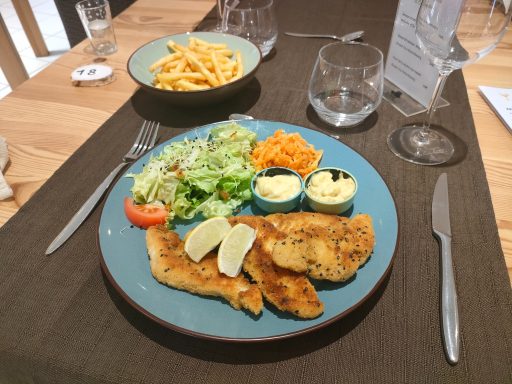 Assiette avec filet de poisson, salade, carottes, sauce et quartiers de citron. Frites en arrière-plan.