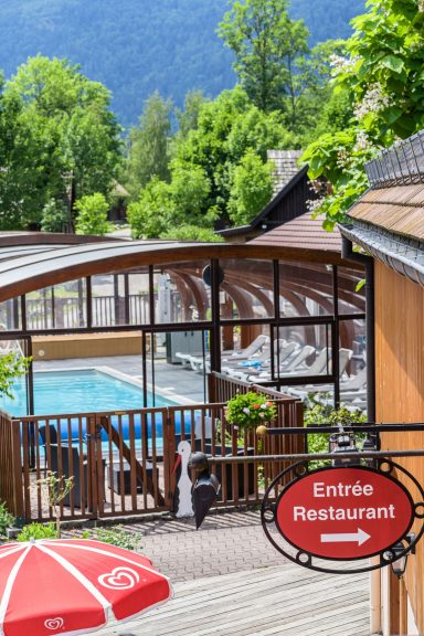 Restaurant près d'une piscine, avec des arbres en arrière-plan et une terrasse.