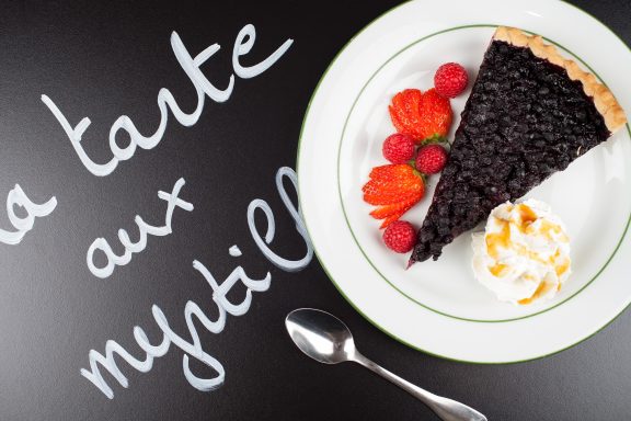 Une part de tarte aux myrtilles avec des fraises et de la crème chantilly sur une assiette.