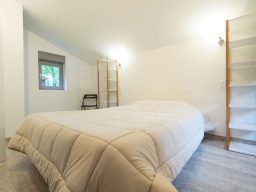 Chalets de la Wormsa et son restaurant Chambre spacieuse avec lit beige, étagère en bois et lumière douce.