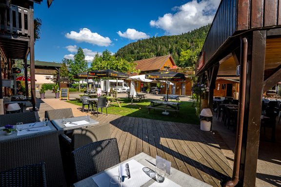 Terrasse du restaurant en plein air avec tables, verdure et ciel bleu.