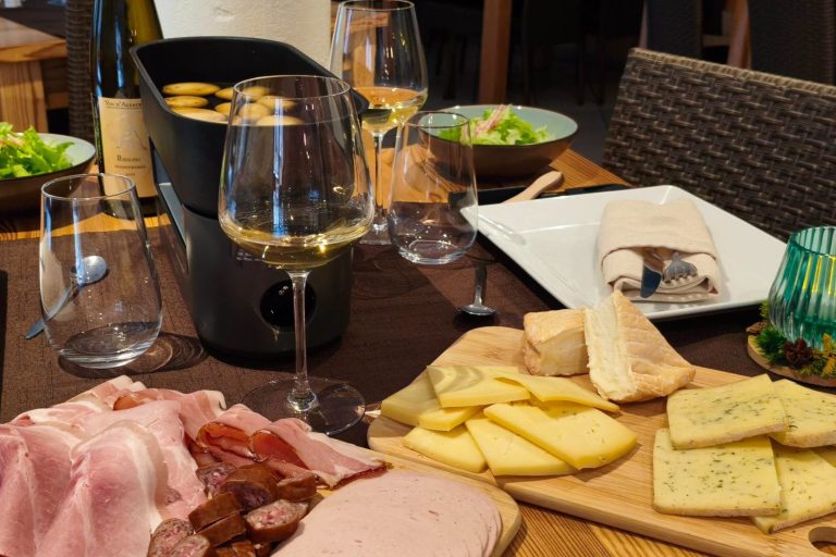 Raclette aux fromages fermier Table dressée avec charcuterie, fromages, salade et verres de vin blanc.