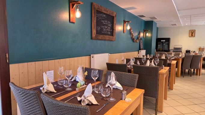 Salle de restaurant avec tables dressées et mur vert décoré.