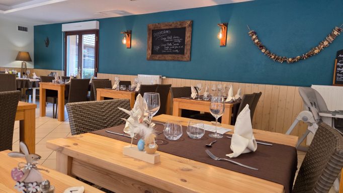 Intérieur de restaurant avec tables en bois, nappes pliées et décor chaleureux.