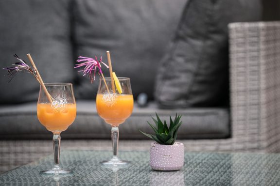Deux cocktails orange avec des parasols sur une table en verre et une plante en pot.