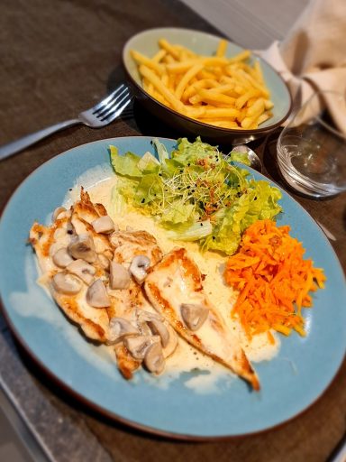 Plat de poulet grillé avec purée, salade, carottes râpées et frites à côté.