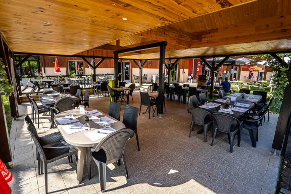 Terrasse d'un restaurant avec tables et chaises noires sous une structure en bois.