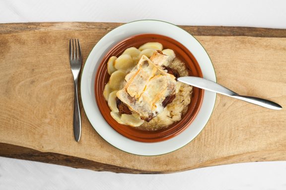 Plat de gratin de pommes de terre avec viande sur un fond en bois.