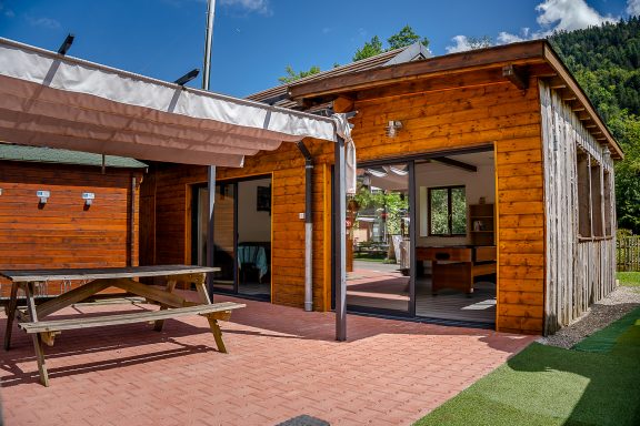 Bâtiment en bois avec véranda, table de pique-nique et vue sur la nature environnante.