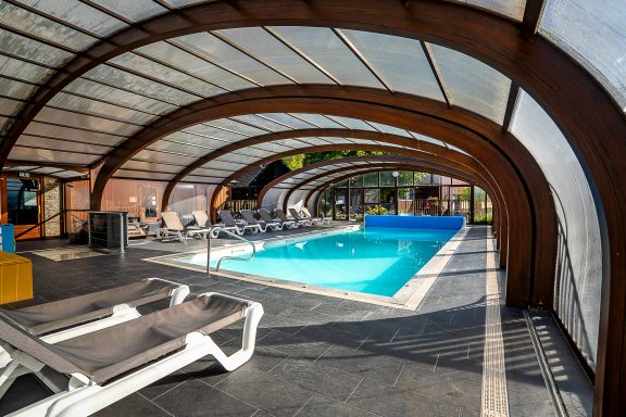 Piscine intérieure avec chaises longues et structure en bois, éclairée par la lumière naturelle.