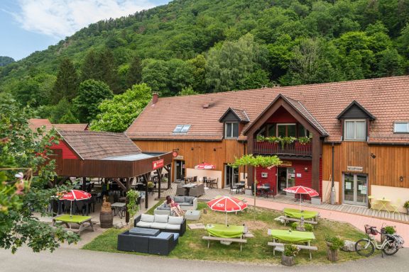 Bâtiment en bois avec terrasses, parasols et verdure environnante.