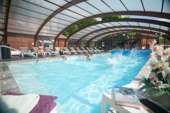 Piscine intérieure avec des transats, des personnes s'amusant et des fleurs décoratives.