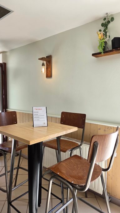 Coin d'un café avec des sièges en bois et une lumière murale douce.