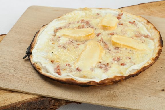 Tarte fine garnie de fromage et lardons sur une planche en bois.