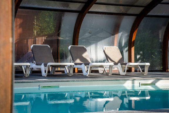 Chaises longues en bord de piscine sous un abri, avec reflection dans l'eau.